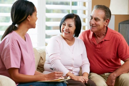 A caregiver sitting and chatting with an older couple at home